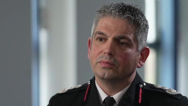 Head and shoulders of Ben Ansell looking serious. He's wearing his fire service uniform - a black blazer with red braids on the collar and silver crests on the epaulettes