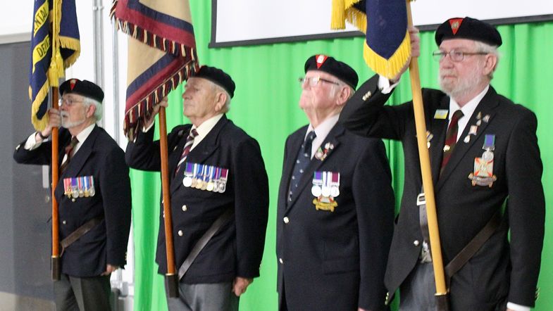 Four members of the Royal British Legion carrying flags on stage 