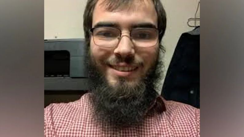 Khaled Hussein has brown hair, a large beard and glasses and a red and white shirt - the picture appears to be a selfie and he is smiling into the camera 