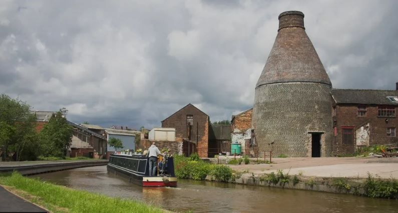 A narrowboat travels along Stoke-on-Trent's canal network past a bottle kiln