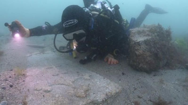 A diver at the sea bed posing with a gravestone stone