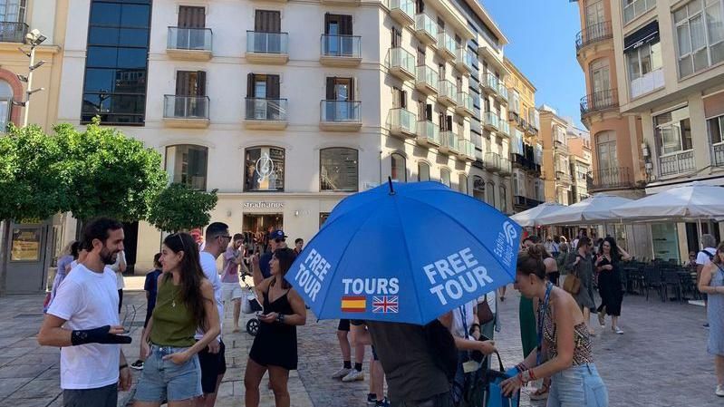 A tour guide, surrounded by tourists, holds an umbrella 