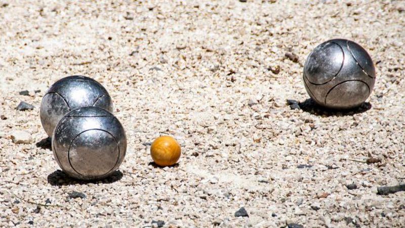 Three shiny metal pétanque boules on a gravel floor