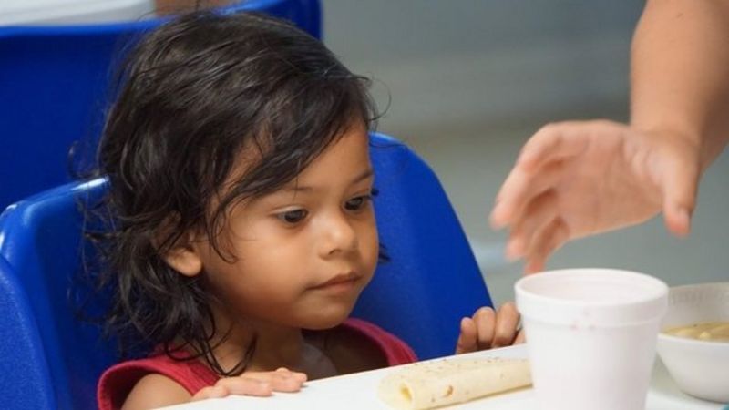Menina sentada se prepara para comer em centro de detenção de imigrantes na cidade fronteiriça de McAllen, no Texas (EUA):