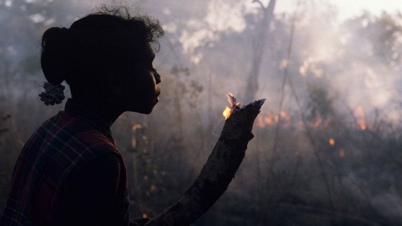 Uma garota em Arnhem Land, na Austrália, segura um pequeno galho em chamas