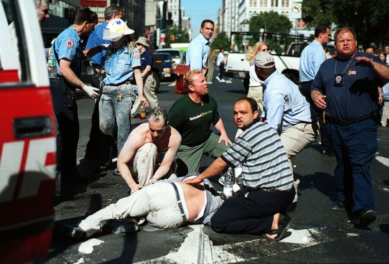 Pessoas na rua e paramédicos atendendo um ferido após o impacto dos aviões nas Torres Gêmeas em Nova York