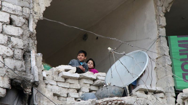 Children look out from a destroyed home in Aleppo, Syria