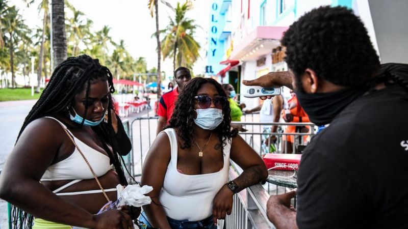 A security guard checks the temperature of a woman at the entrance of a restaurant on Ocean Drive in Miami Beach, Florida, 24 June 2020