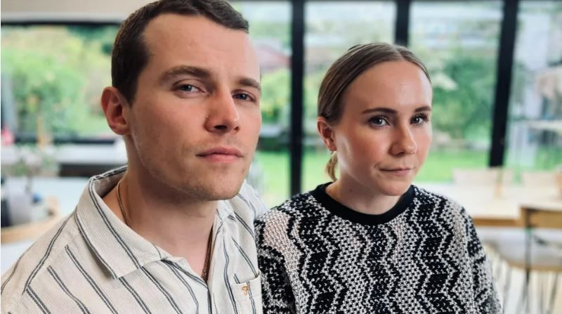 A man and woman sit side-by-side looking into the camera.