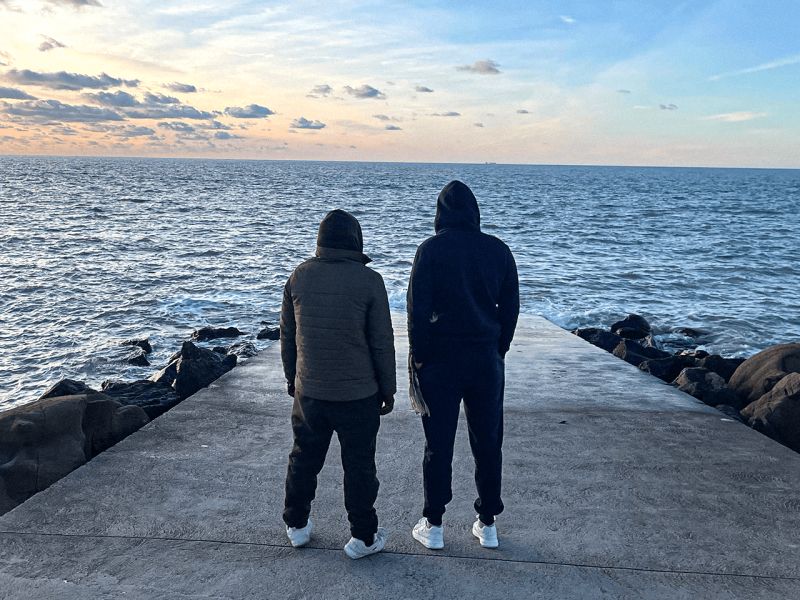 Two men standing with backs to camera, hoods up, looking out to see from the slipway at Wimereux where the deadly incident happened