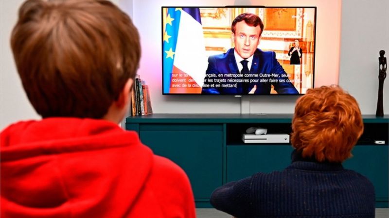 Pessoas assistem ao pronunciamento de Emmanuel Macron na TV