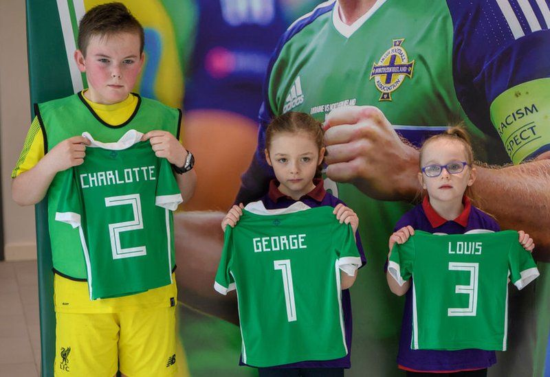 Three children hold NI football shirts for Prince George, Princess Charlotte and Prince Louis.