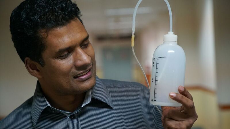 Dr Chisti holding a device made from plastic bottle and tubing