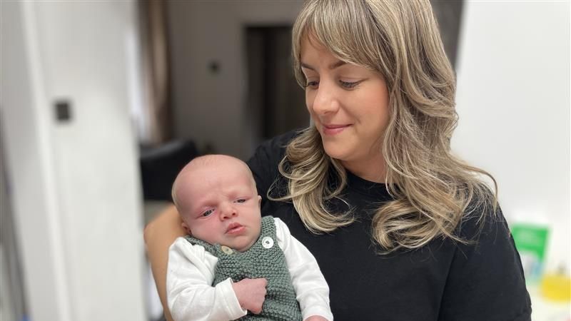 Naomi, wearing a black top, holding Benson in green knitted top.