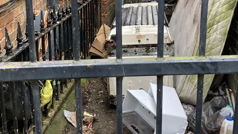 Rubble dumped in an alley in Northampton behind a fence