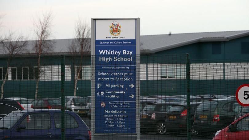 Whitley Bay High School sign with the school building and parked cars in the background.