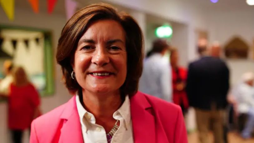 Eluned Morgan wearing white blouse and pink blazer and smiling at camera