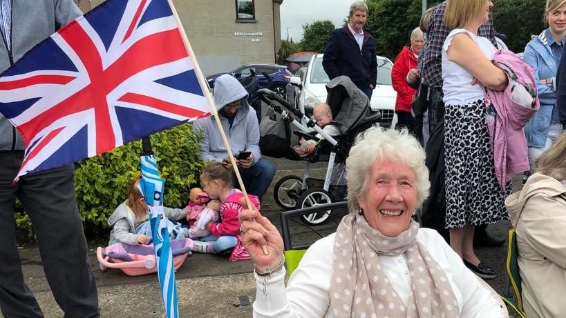 Woman with flag sitting down to watch Limavady parade
