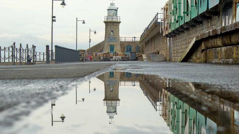 A lighthouse in Folkestone reflecting in a puddle of water 