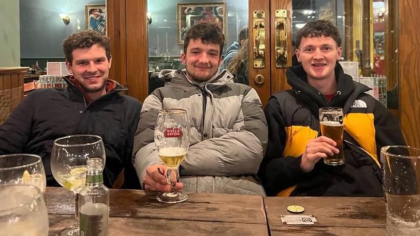 Three men in the pub smiling to camera