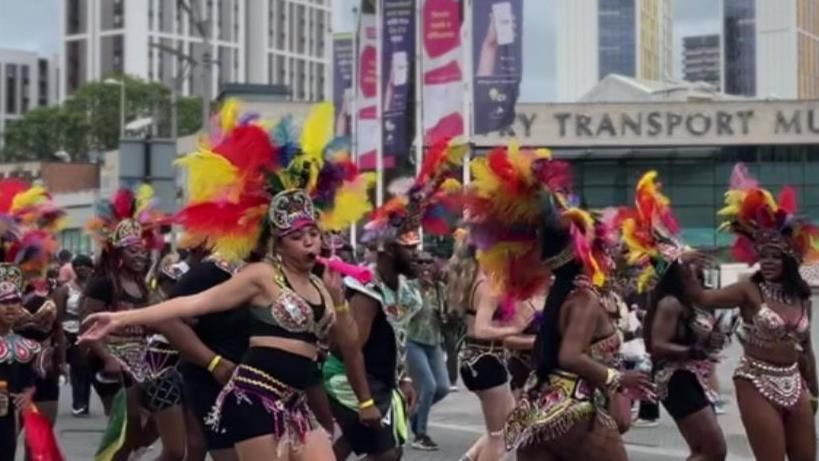 Dancers in a Caribbean parade, they are all wearing bright feathered headdresses