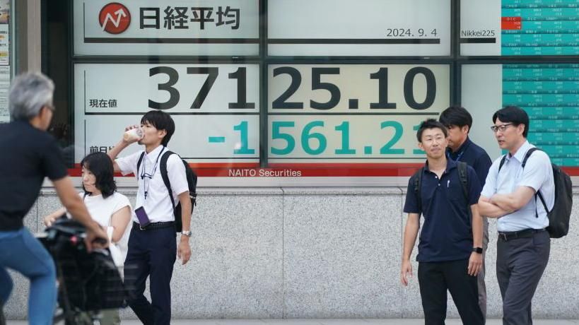 People stand in front of board displaying share prices on the Tokyo Stock Exchange.