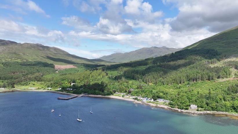 An aerial view of Inverie's white walled properties next to the sea and a below tree covered hill