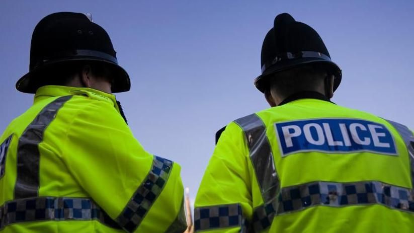 Backs of two police officers in yellow high visibility jackets