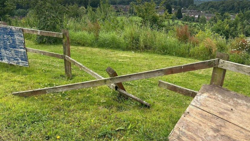 A smashed fence with planks of wood lying on the grass