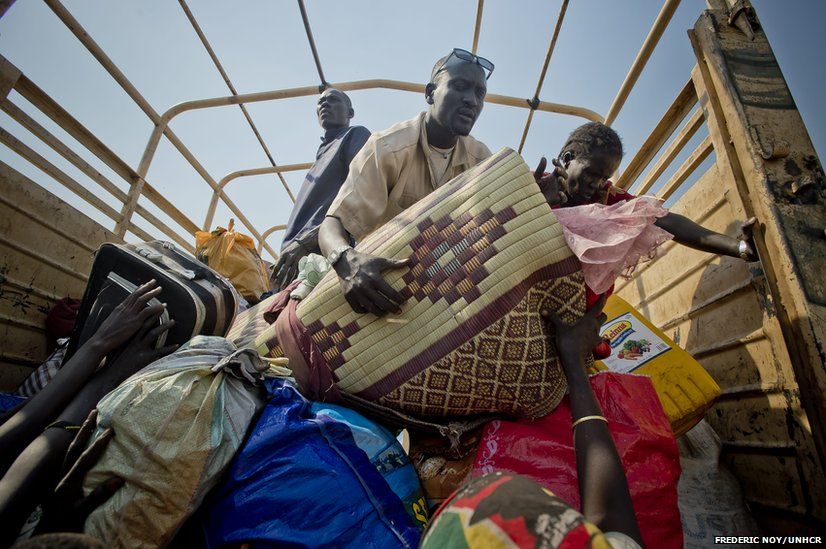 Matiop’s wife hands a sleeping mat to him on a truck, one of many shuttling 100 people at a time away from the South Sudan border.