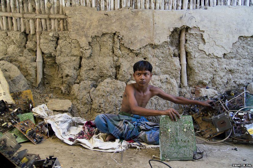 Kochimuni, 15, sits in front of his mud house sorting E-waste and breaking down motherboards into simpler components.