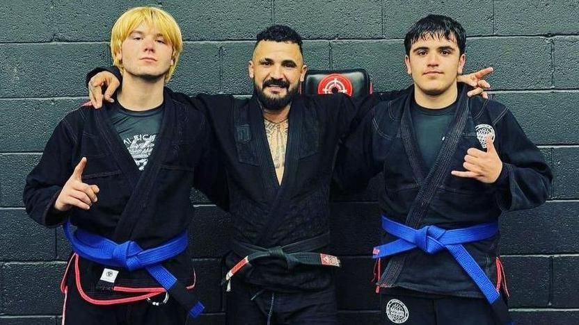 Three men wearing jiujitsu gis, photographed in front of a black wall