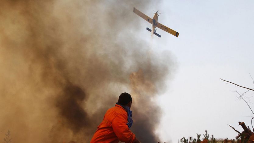 Un hombre rodeado de humo y una avioneta en el cielo