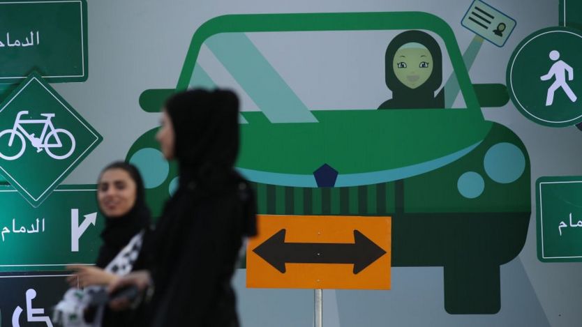 Perempuan berjalan melewati gambar perempuan mengemdui di Jeddah, Arab Saudi.
