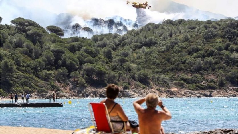 People sit on the beach as they look at Canadair aircraft dropping water over a fire in La Croix-Valmer, near Saint-Tropez. Photo: 25 July 2017