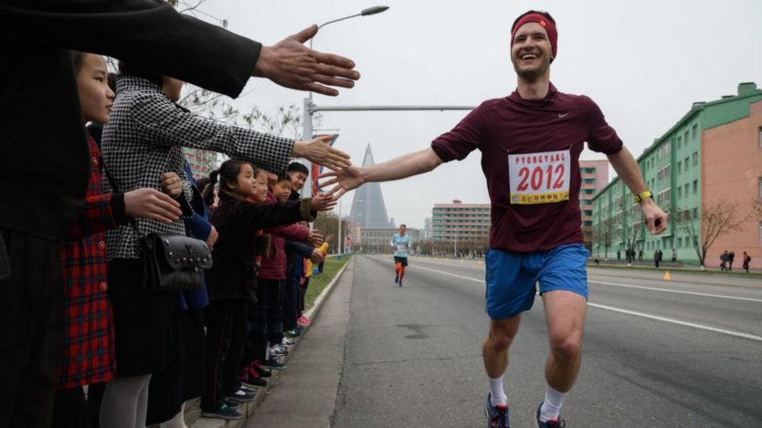 A foreign runner high-fives North Koreans as he runs the marathon