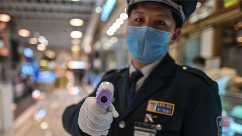 Un guardia de seguridad en China con un termómetro en la mano.
