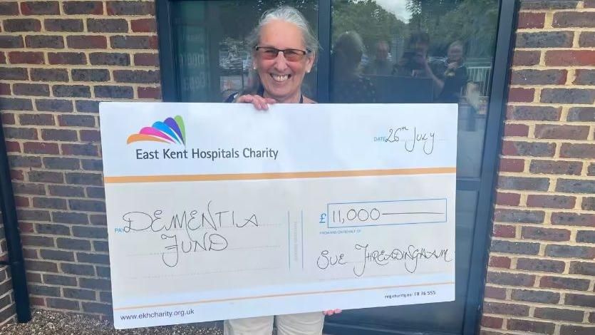 Sue Threadingham with a large cheque for £11,000 made out to the dementia fund at the East Kent Hospitals Charity. She is holding the cheque and smiling