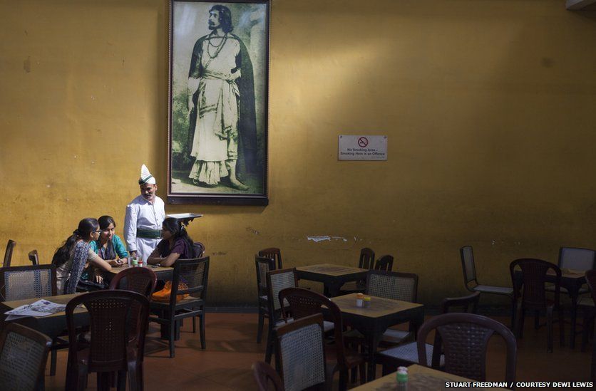 A waiter serves schoolgirls beneath a portrait of Rabindranath Tagore in the Indian Coffee House, Kolkata, India