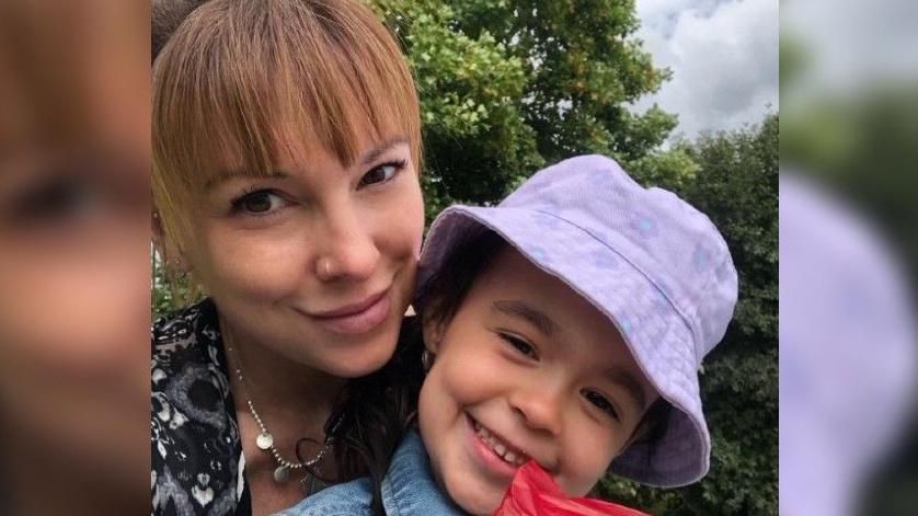 Mum smiling with sparkling black and white top, cuddling her son with purple hate, who is also smiling.