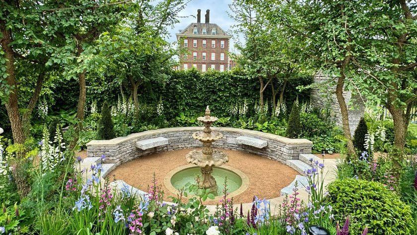 The bridgertnon garden with a water feature in the middle of a walled seating area. There are flowers in shades of blue, purple and pink. 