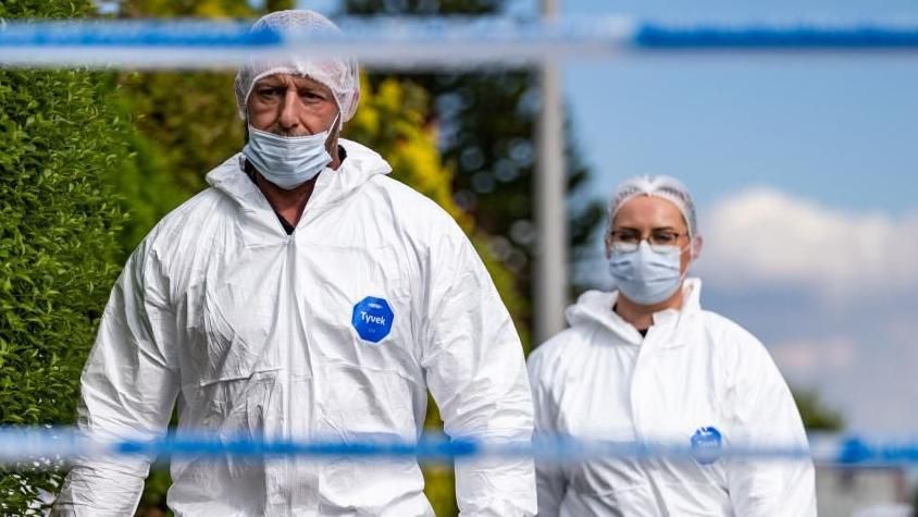 Forensic workers in hazmat suits at the seen of a stabbing attack in Southport. In the foreground of the image is police tape.