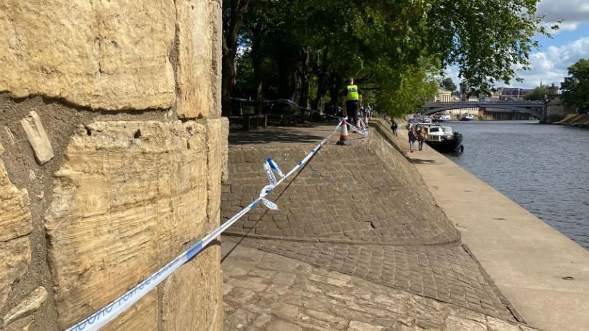 Police tape runs alongside riverside path 