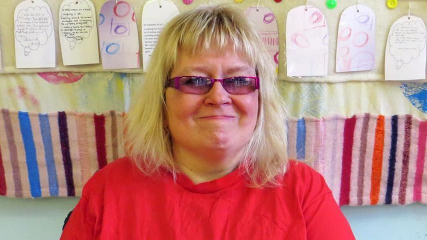 Angela Chadwick, smiling, in a red T-shirt and glasses