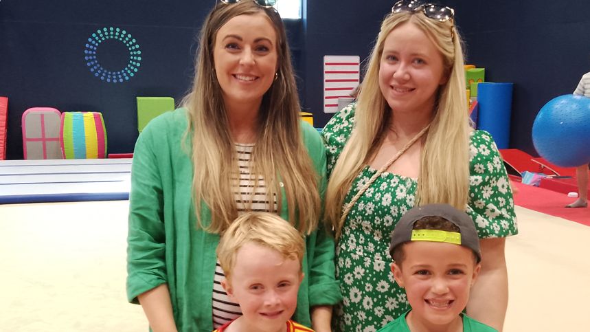 Joanna, Samantha, Carter and Zach. Zach is wearing red. Carter is in green and is wearing a baseball cap. Samantha is wearing  a green flowery dress. Joanna is wearing a green cardigan with a stripped top.