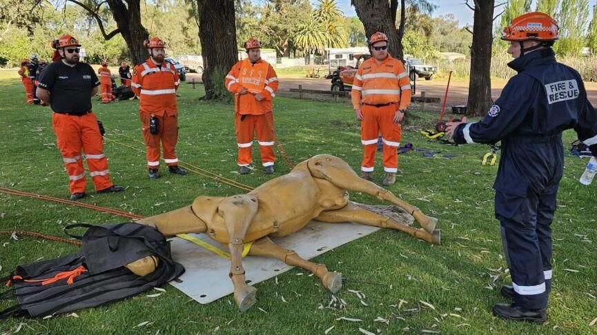 Four firefighters and an instructor look at a model of a horse lying on the floor