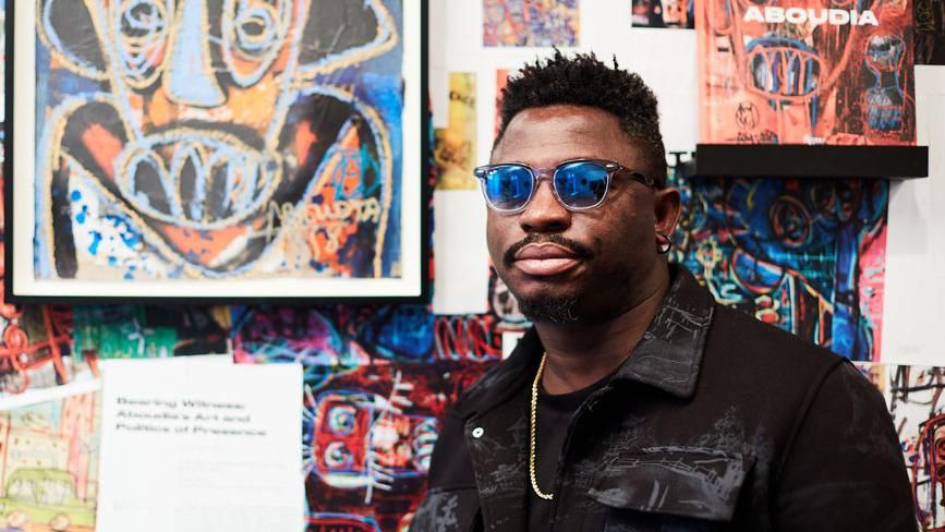 Ivorian artist Aboudia stands in front of his paintings