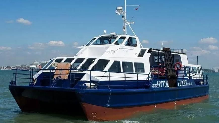 Blue and white Hythe Ferry in the water with Southampton docks in the background