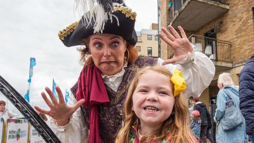A woman in pirate fancy dress stands behind a smiling little girl during the foyle maritime festival