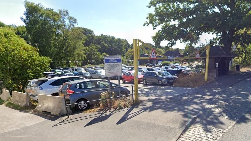 Cars are parked in a car park with a yellow entrance barrier